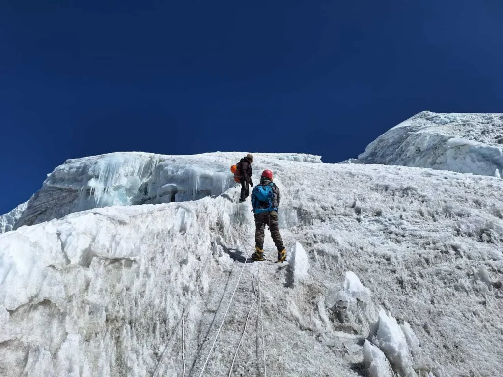 Trekker climbing Lobuche Peak under a clear open sky, using a rope on the steep icy slope