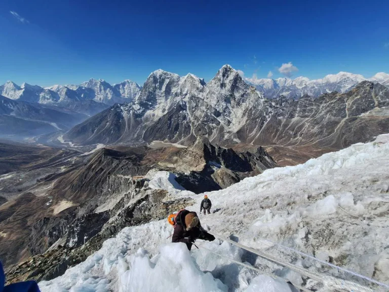 Trekker climbing Lobuche Peak with rope support against a backdrop of snowy mountain terrain
