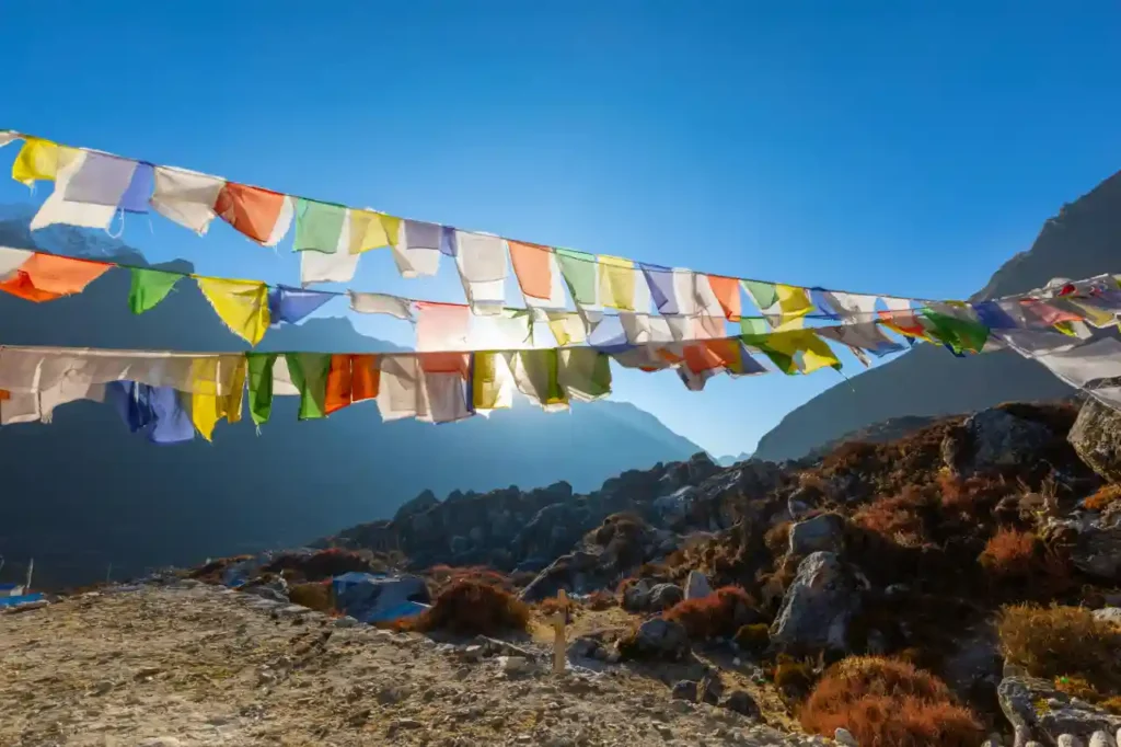 A wide-angle landscape shot of colorful Tibetan prayer flags hanging in rows across a rugged mountain terrain.