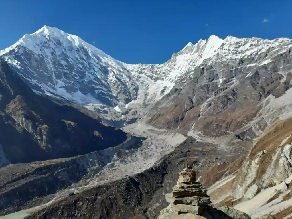 A wide-angle landscape photograph featuring towering, snow-covered mountain peaks under a clear, deep blue sky.